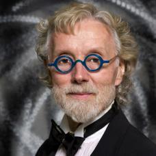 Man with blond hair, beard and mustache and blue round glasses in a suit and bowtie