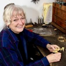 Female sits at a table, smiling with some of her jewelry in her hands